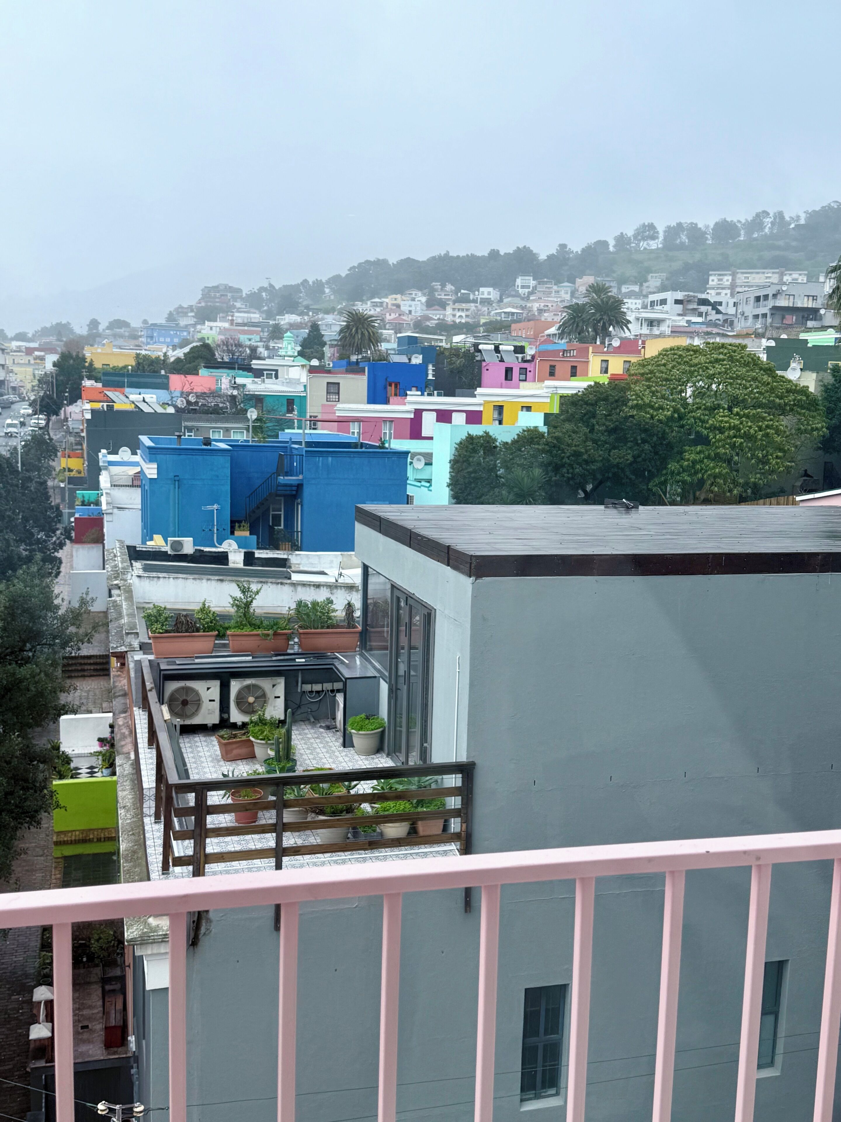 Un barrio residencial con edificios coloridos, un balcón con plantas en macetas y vistas de la ciudad.