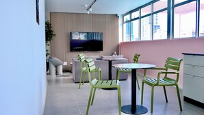 A modern interior with a TV mounted on a wooden wall, green chairs around a small table, and a pink wall. - Urban Elephant The Rose (Cape Town)