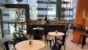 A café with round tables and black chairs, a bar area with a statue, and large windows offering a view of the street. - Urban Elephant The Rose (Cape Town)