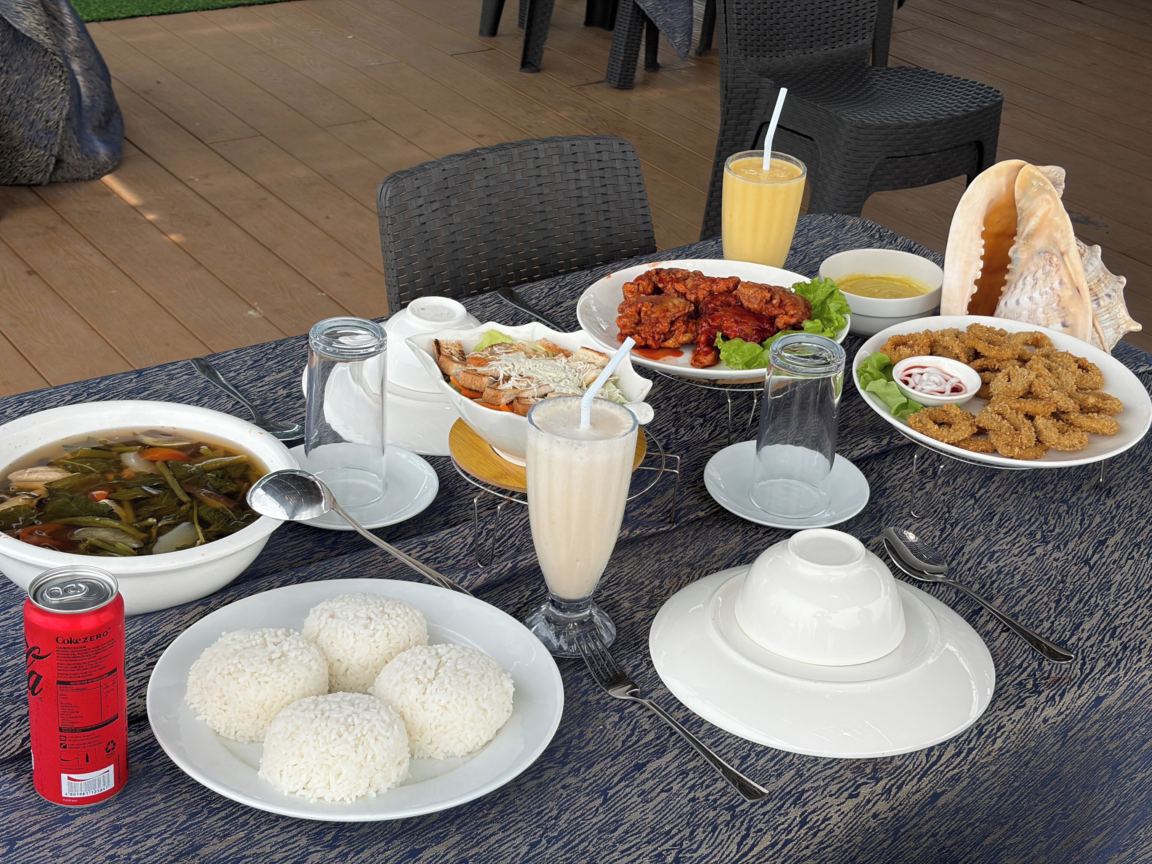 A table set with various dishes, drinks, and a can of soda.