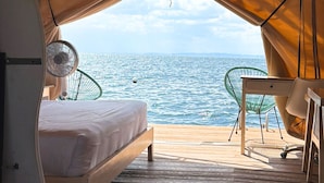 A tent with a bed, a table, and a chair, with a view of the sea. - Floating Home in Reef Resort Unit 1 (Samal)