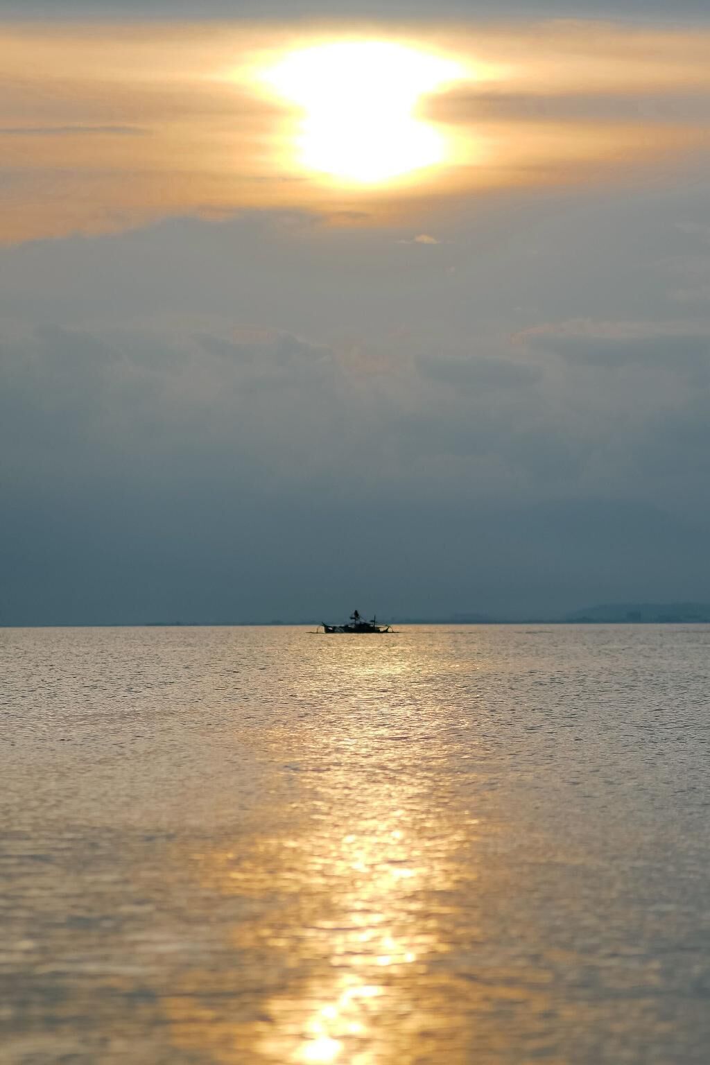 A calm sea with a boat in the distance and a bright sun near the horizon.