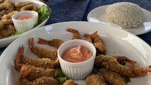 A dining table with a plate of breaded shrimp and rice, a bowl of dipping sauce, and a shell on the table. - Floating Home in Reef Resort Unit 1 (Samal)