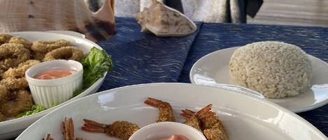Une table à manger avec une assiette de crevettes panées et du riz, un bol de sauce pour tremper, et une coquille sur la table.