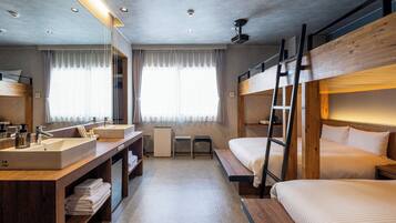 A modern hotel room with bunk beds, a large mirror, a wooden vanity with a sink, and a ceiling projector.