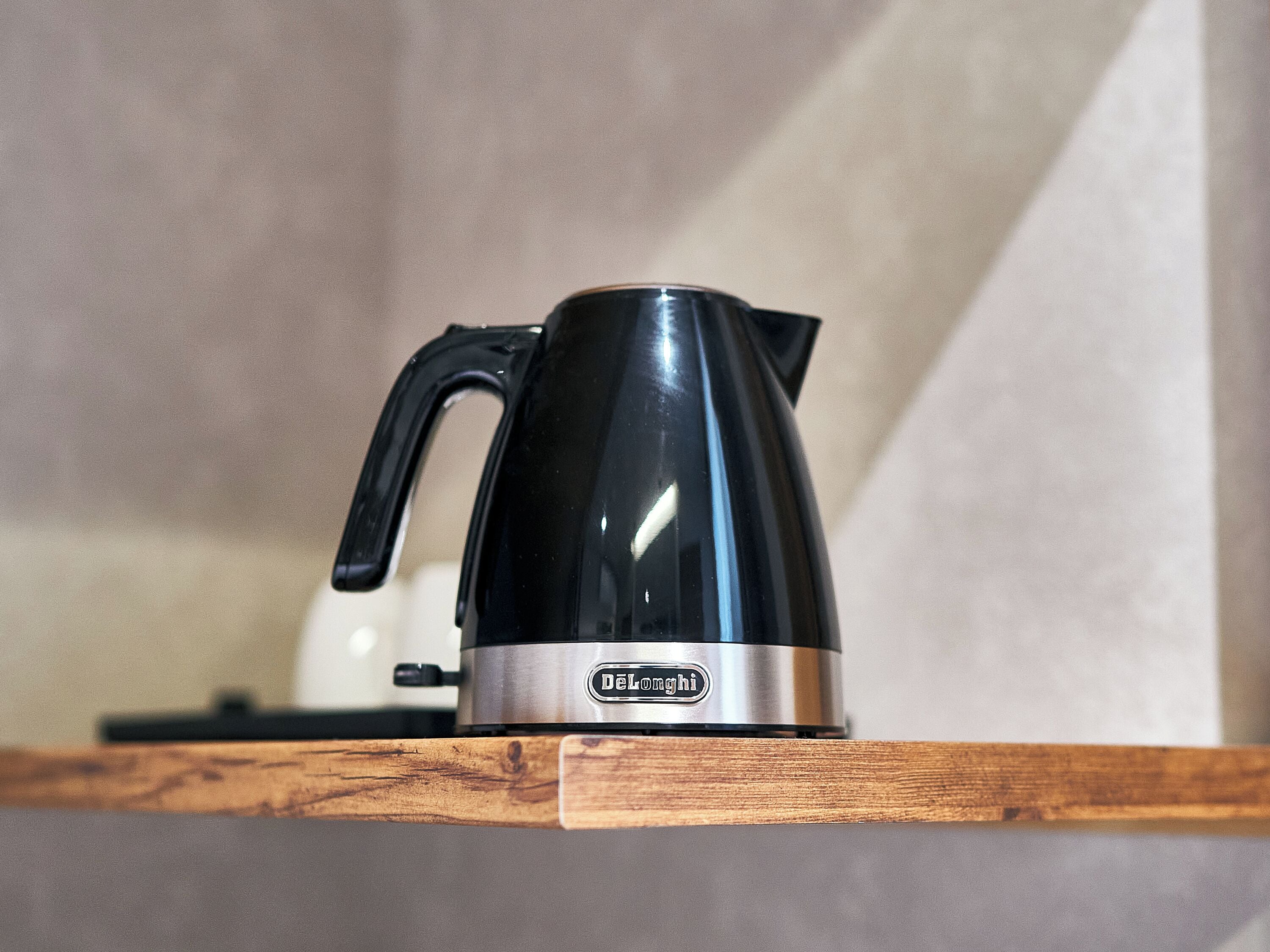 Una tetera eléctrica negra con base de acero inoxidable sobre un estante de madera.