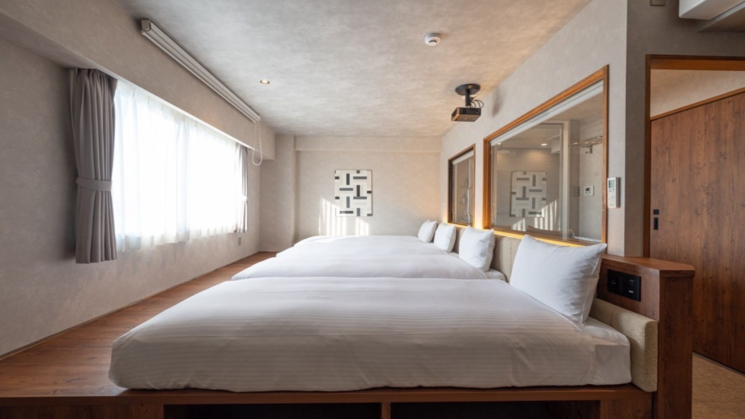 Una habitación de hotel moderna con una cama grande, un banco de madera, un espejo y una ventana con cortinas.