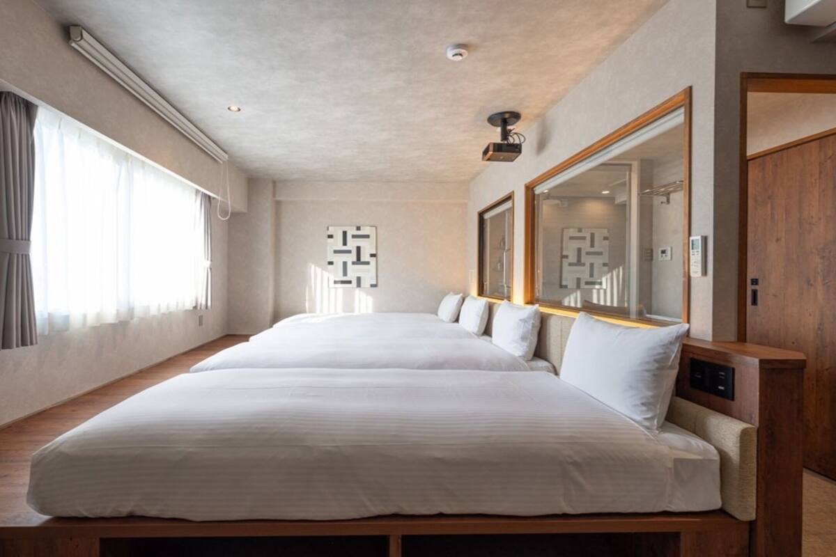 Ein modernes Hotelzimmer mit einem großen Bett, einer hölzernen Bank, einem Spiegel und einem Fenster mit Vorhängen.