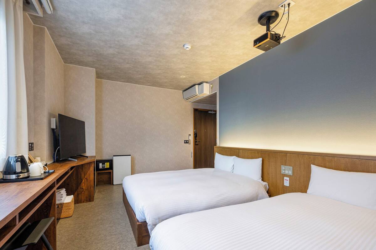 Ein Hotelzimmer mit zwei Betten, einem Schreibtisch, einem Fernseher, einer Kaffeemaschine und einem kleinen Kühlschrank.