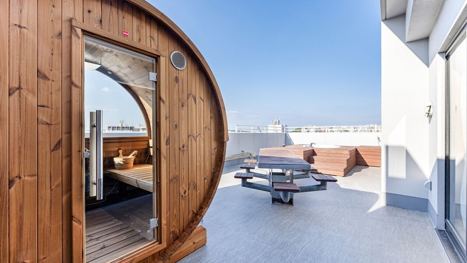 Une structure en bois dotée d’une porte en verre, d’une table ronde et offrant une vue sur le paysage urbain.
