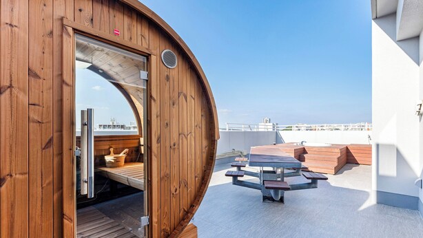 Un sauna en bois doté d’une porte en verre, d’une terrasse en bois et d’une table avec des bancs.