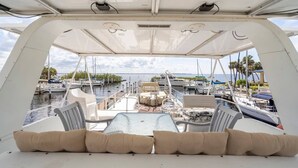 A boat deck with a table and chairs, a cushioned bench, and a view of the marina with other boats. - 62' Yacht M/v Possibilities On Wide Private Canal 3 Bedroom Houseboat (North Fort Myers)