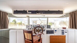 A boat's control station with a steering wheel, multiple control panels, and a view of the outside through large windows. - 62' Yacht M/v Possibilities On Wide Private Canal 3 Bedroom Houseboat (North Fort Myers)