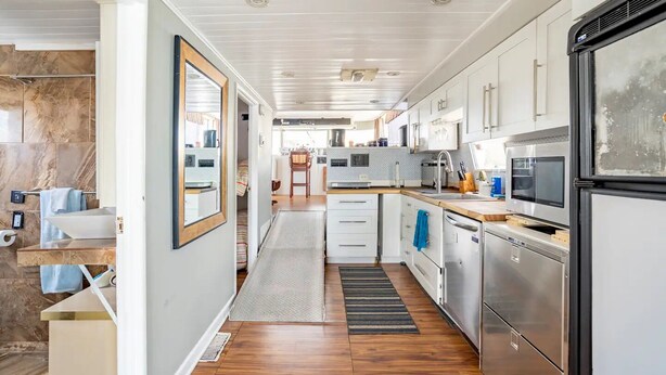 A modern kitchen with white cabinets, stainless steel appliances, and a wooden floor. - 62' Yacht M/v Possibilities On Wide Private Canal 3 Bedroom Houseboat (North Fort Myers)