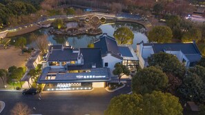 A hotel with a modern design, featuring a large glass facade, a parking area, and a landscaped garden with a pond. - UrCove by Hyatt Shanghai Dishui Lake (Shanghai)