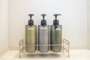 Tre bottiglie di shampoo, balsamo e sapone corpo su un ripiano metallico.