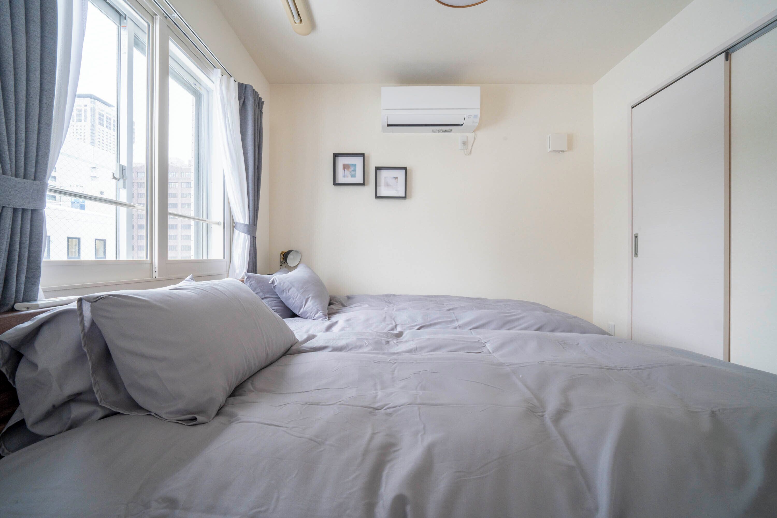 A bedroom with a bed, window, air conditioning unit, and two framed pictures on the wall.
