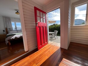A room with a wooden floor, a red door, and a view of an outdoor patio with a table and chairs. - Sackville Retreat (2 min walk to Square), Close to town and short walk to Vineyards (Martinborough)