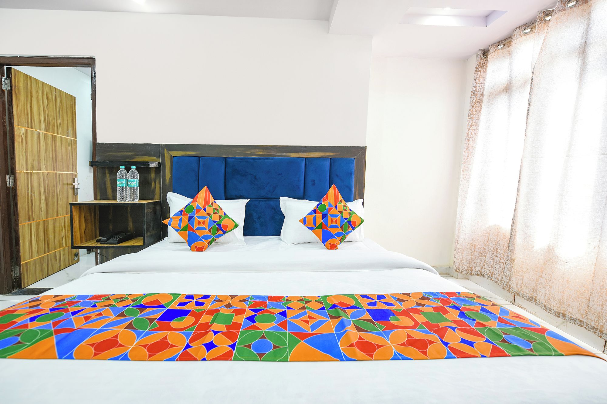 Habitación de hotel con cama, dos almohadas, armario de madera y ventana con cortinas.