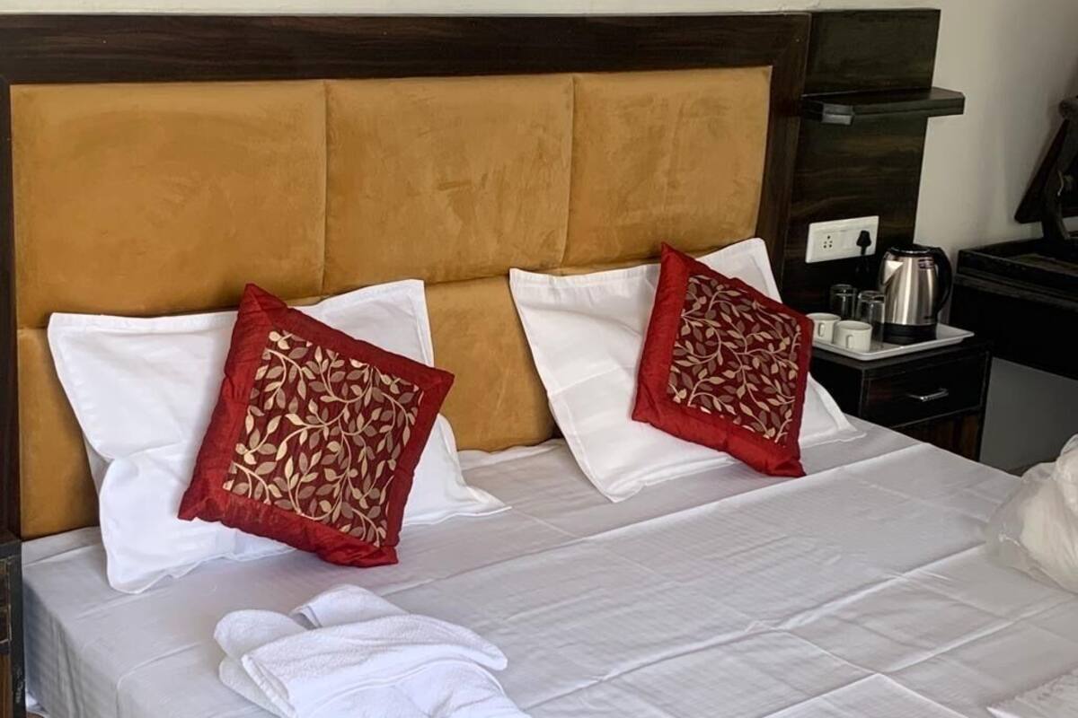 A neatly made bed with white and red pillows, a wooden headboard, and a bedside table with a kettle and cups.
