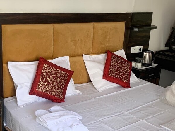 A neatly made bed with white and red pillows, a wooden headboard, and a bedside table with a kettle and cups. - Beer Castle Hotel  (Theog)