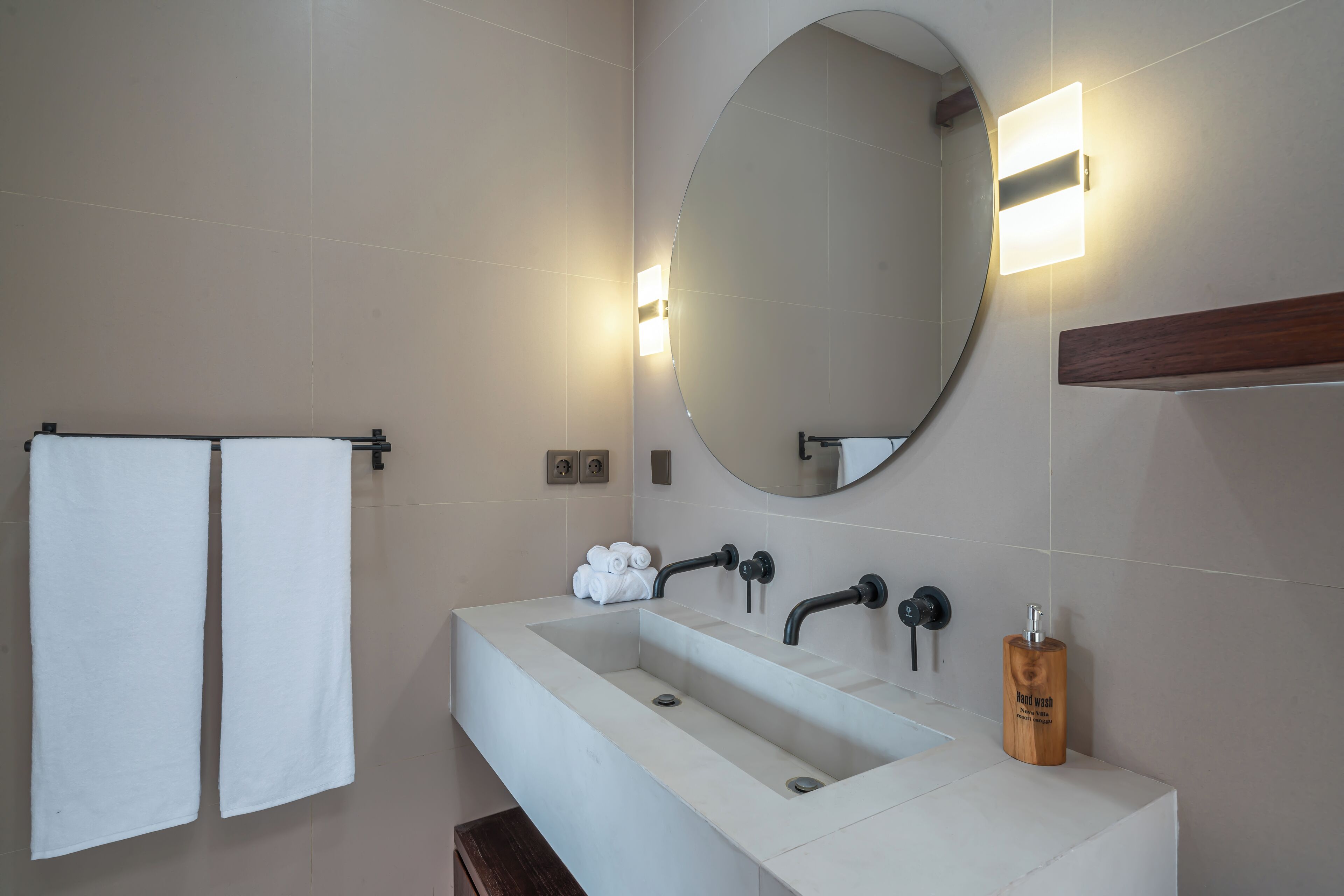 A modern bathroom with a large rectangular sink, a round mirror, and two wall-mounted towel racks.