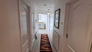 Un couloir aux murs blancs, avec un tapis à motifs et une porte sur le côté droit.