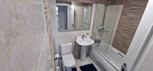 A compact bathroom with a toilet, sink, and glass shower enclosure.