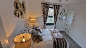 Habitación de hotel con cama, dos lámparas de noche, ventana con cortinas, espejo y radiador.