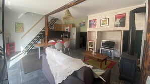Uma sala de estar moderna com um sofá, uma mesa de jantar e uma lareira. Uma escadaria leva a um andar superior.