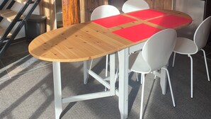 Uma cozinha moderna com escada de madeira, mesa de jantar com cadeiras brancas e geladeira de aço inoxidável.