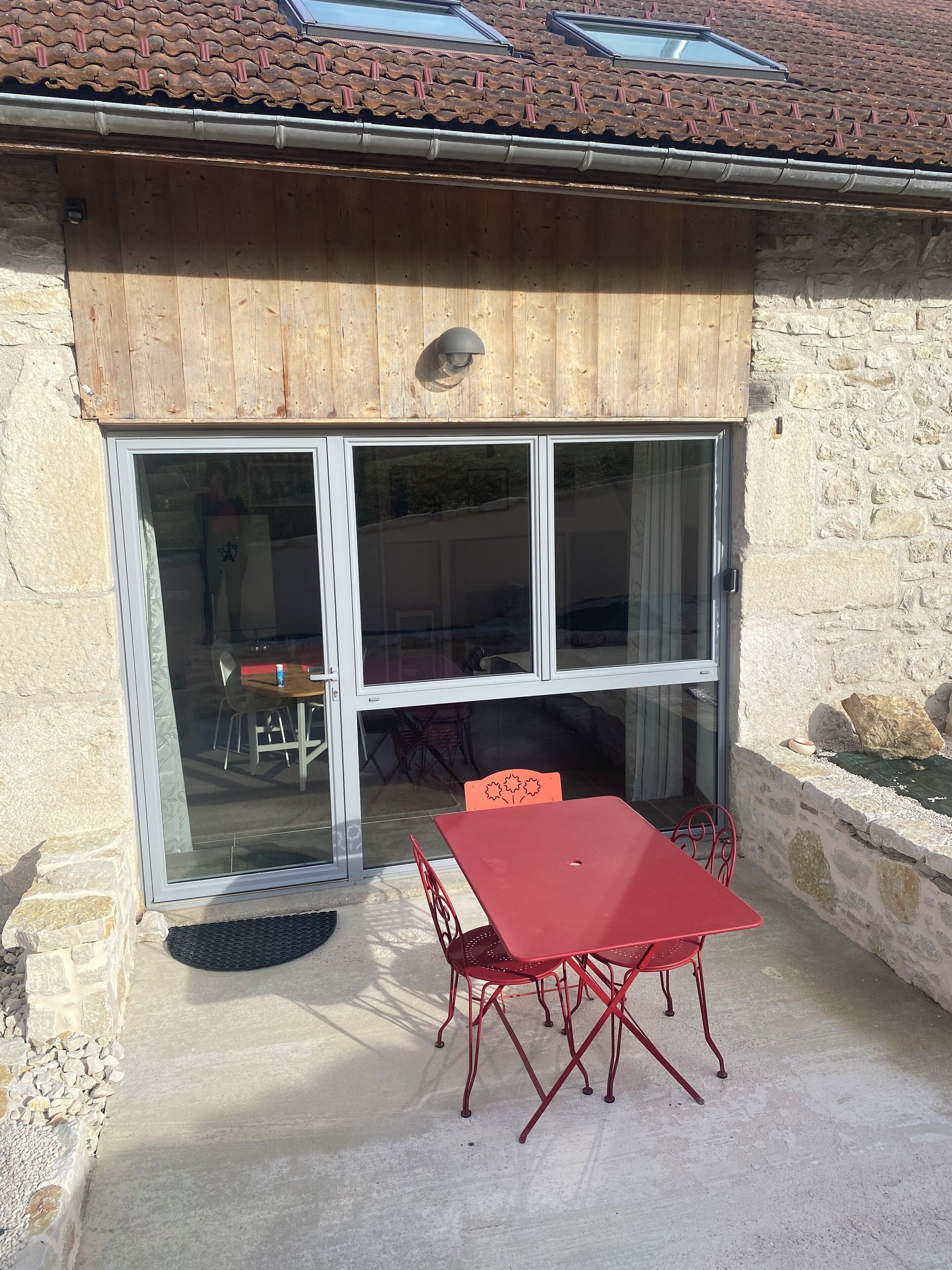 Une terrasse couverte avec une table et des chaises, un mur en pierre et un toit recouvert de tuiles.