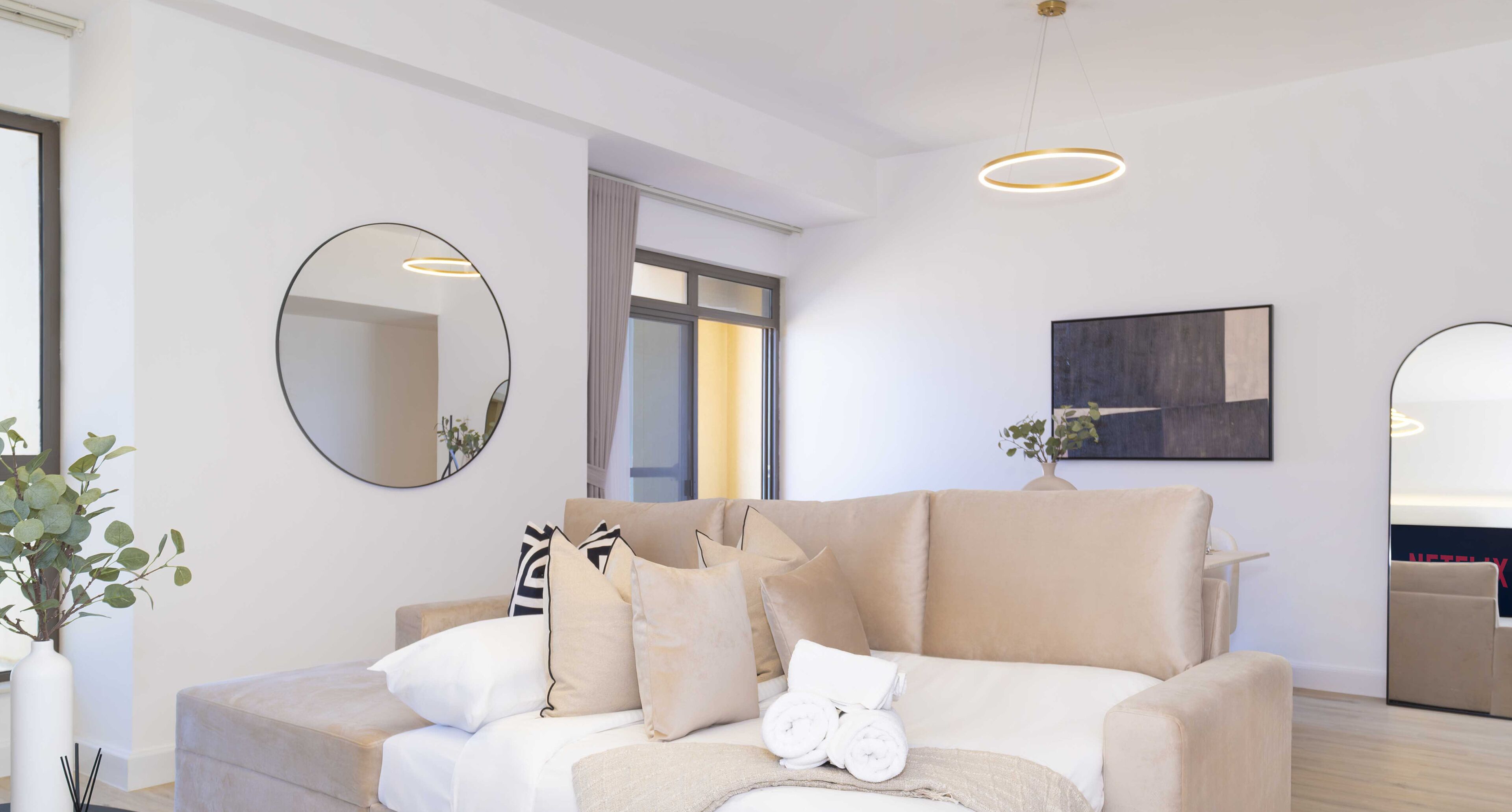 Un salon moderne avec un canapé beige, un miroir rond et une décoration minimaliste.