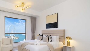 A hotel room with a large window, a bed with white linens, a headboard, a bedside table with a lamp, and a view of a Ferris wheel. - LUX  The Dubai Eye Sea View Suite (Dubai)