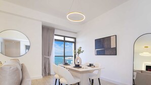A modern dining area with a table, chairs, and a view of the sea through large windows. - LUX  The Dubai Eye Sea View Suite (Dubai)