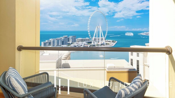A balcony with wicker chairs and a view of a cityscape including a large Ferris wheel and cruise ships. - LUX  The Dubai Eye Sea View Suite (Dubai)