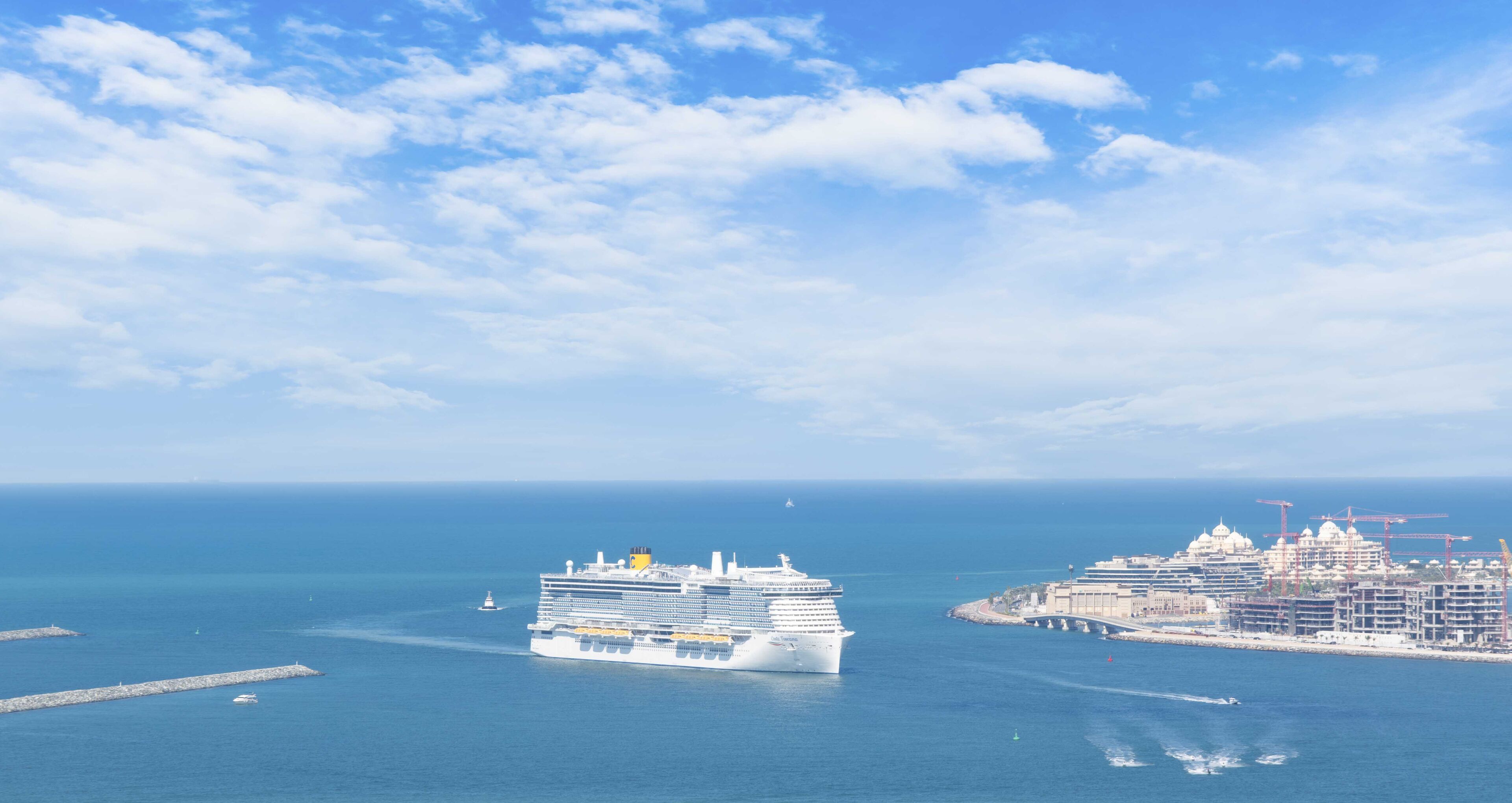 Un gran crucero amarrado cerca de un puerto, con un paisaje urbano al fondo.