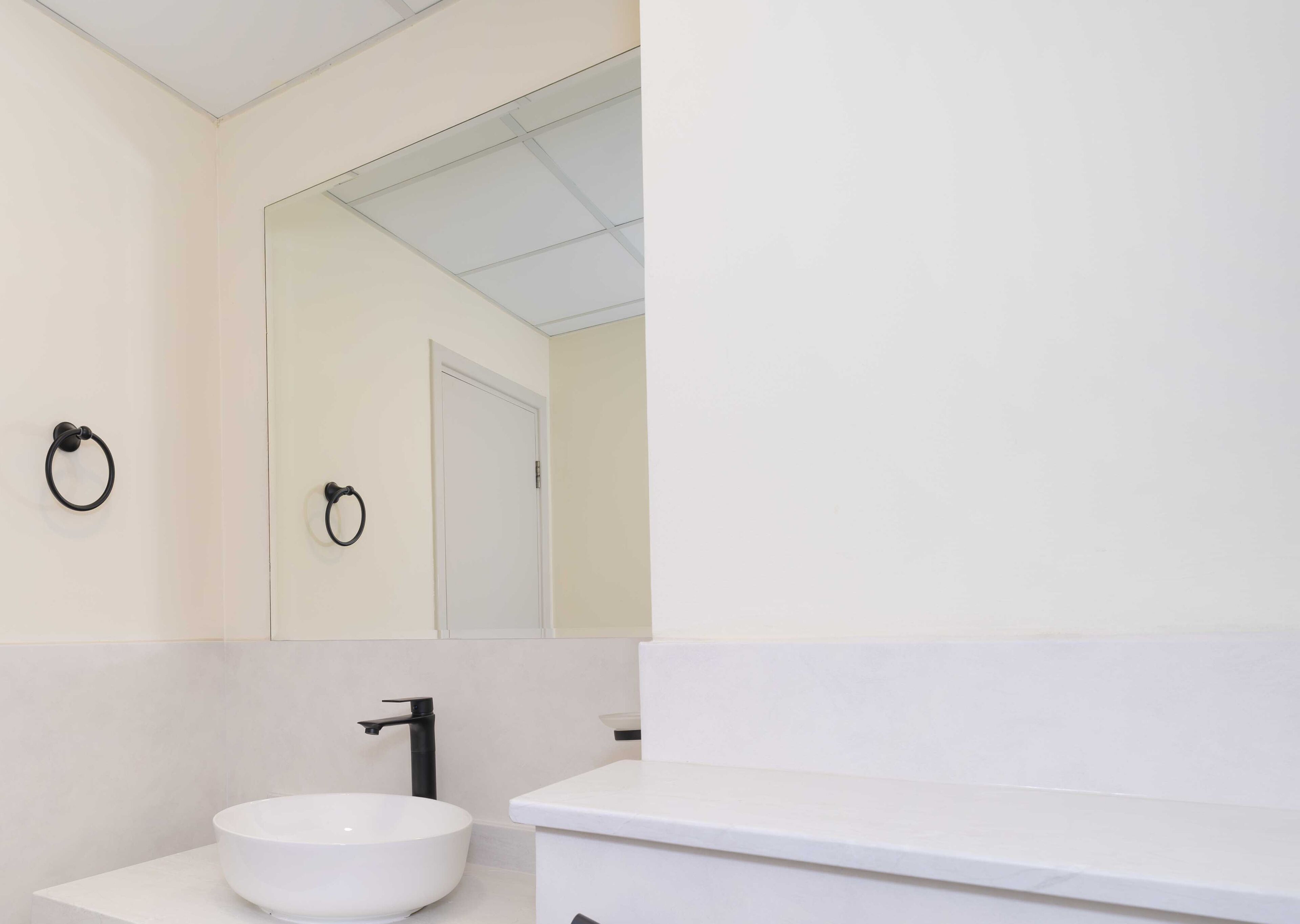 A modern bathroom with a white sink, black faucet, and a mirror reflecting a door.