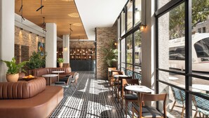 A modern interior with leather seating, a patterned floor, and large windows offering views of the street. - Hotel Bazaar - Fattal Colors (Tel Aviv)