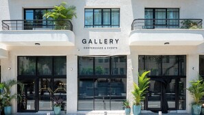 A building with a sign reading 'GALLERY CONFERENCES & EVENTS' and balconies with potted plants. - Hotel Bazaar - Fattal Colors (Tel Aviv)