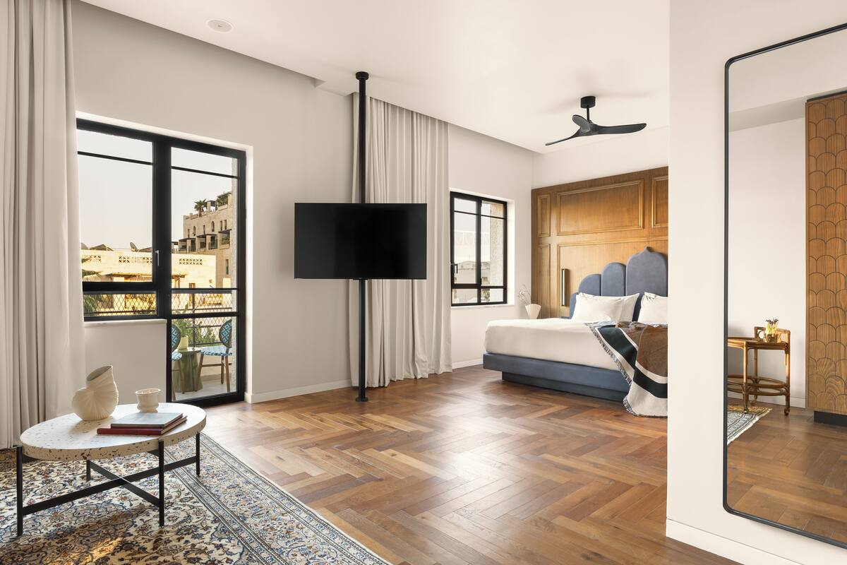 A modern hotel room with a large bed, a flat-screen TV, and a view of the cityscape through large windows.