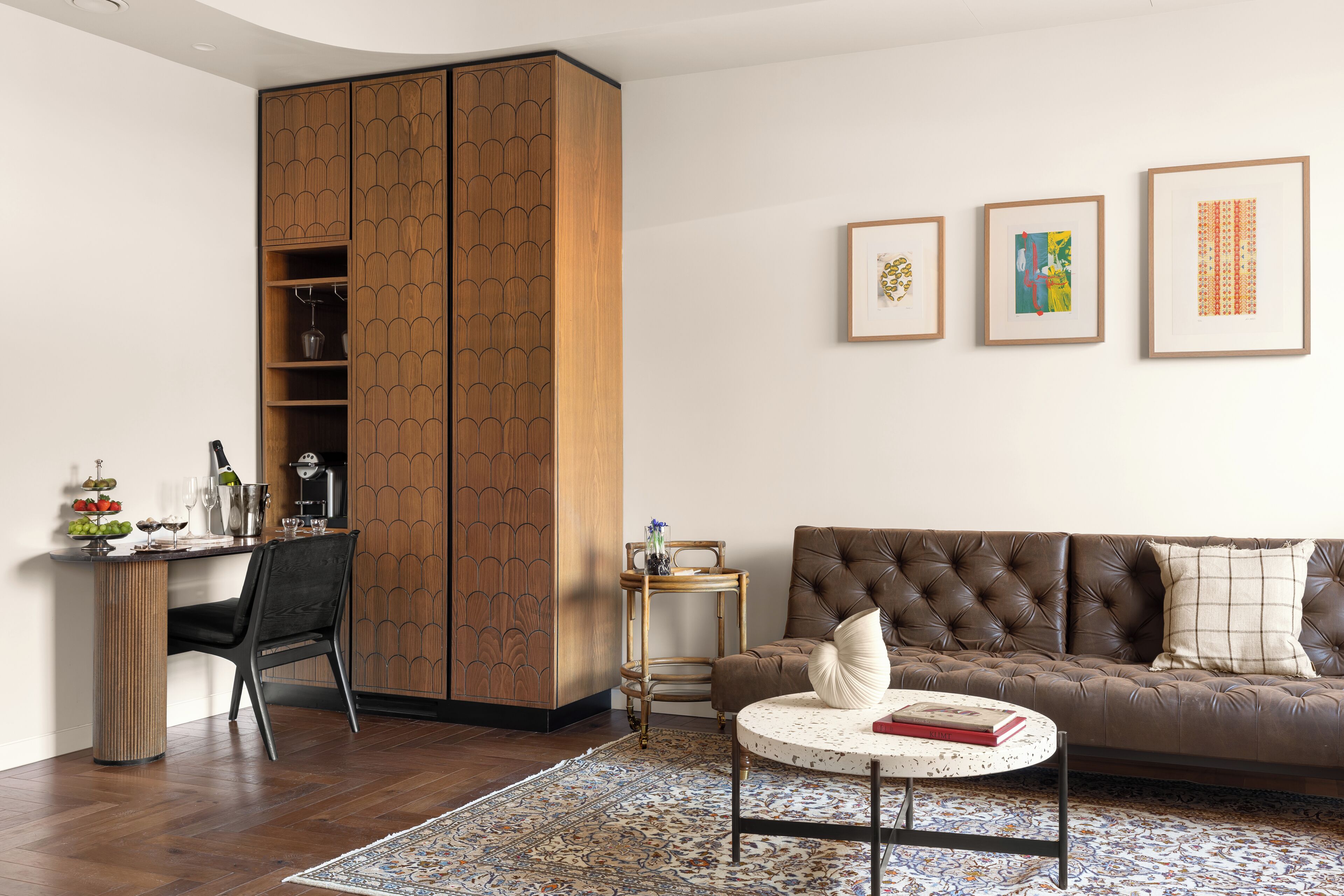 Una sala de estar moderna con un sofá de cuero marrón, una mesa de centro redonda, un aparador de madera y una mesita auxiliar.