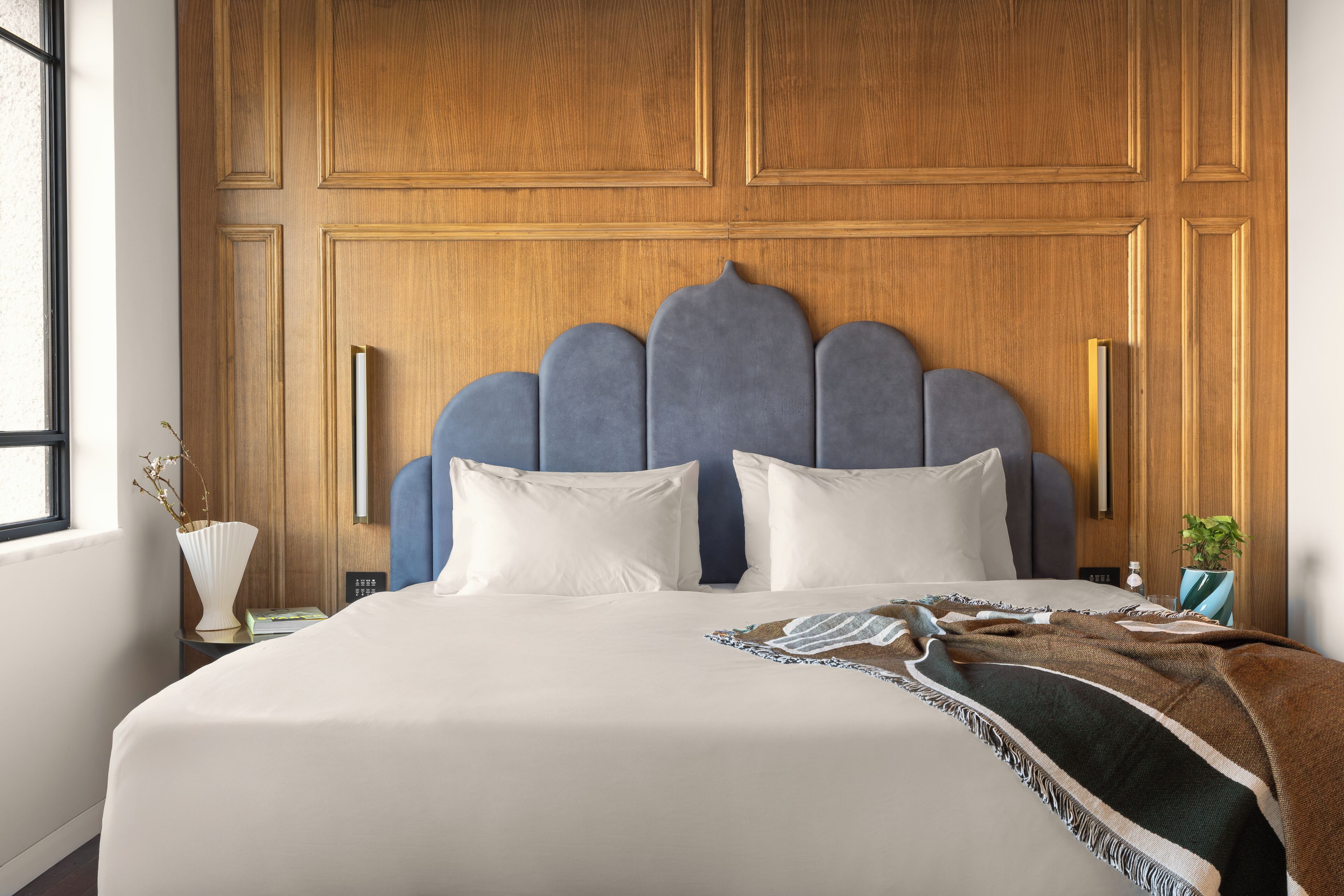 Cama bem arrumada com cabeceira azul, travesseiros brancos e manta listrada.