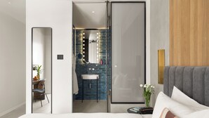 A modern hotel room with a large bed, a bedside table, a mirror with lights, a sink, and a wooden panel on the wall. - Hotel Bazaar - Fattal Colors (Tel Aviv)