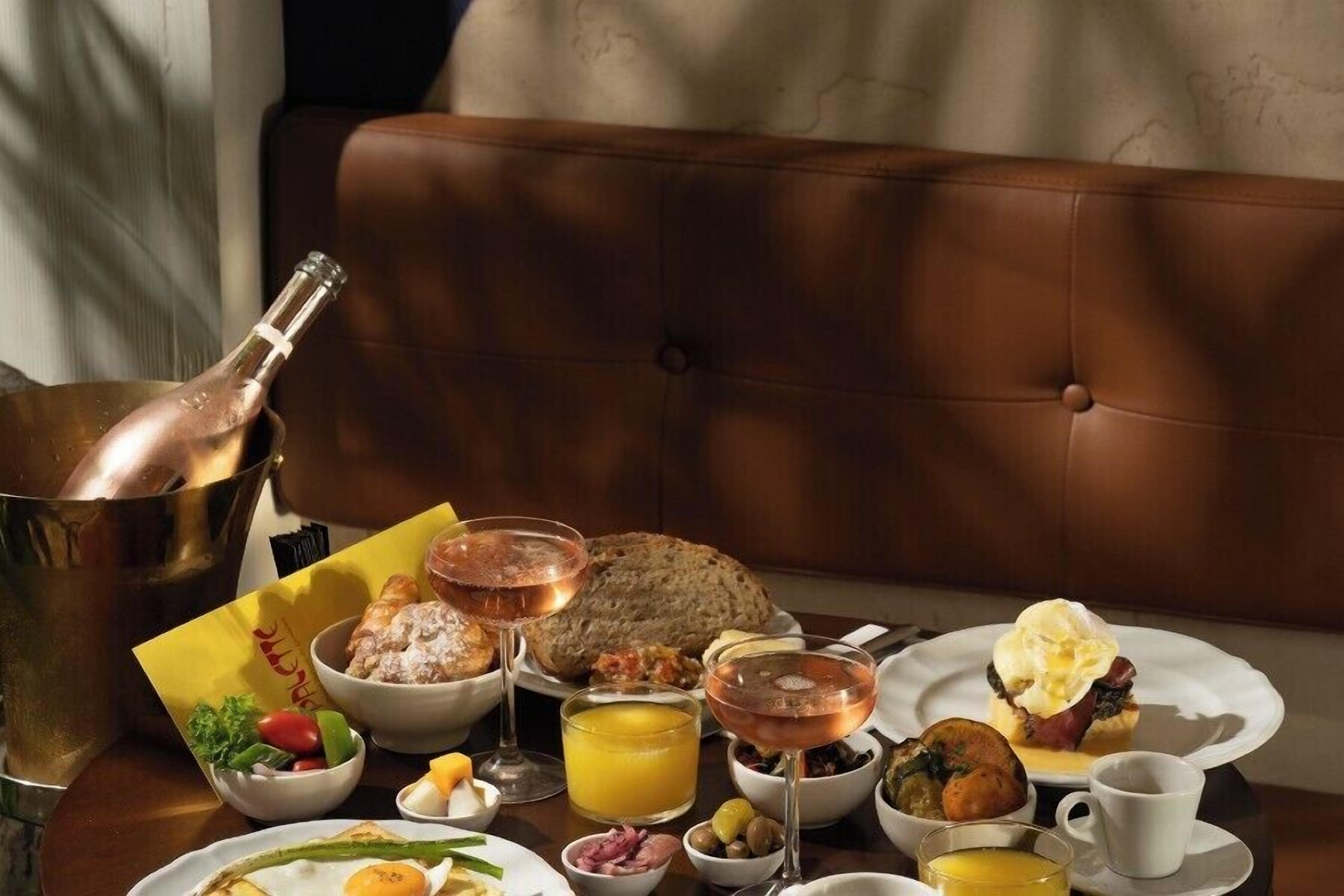 A breakfast setting with a variety of dishes, drinks, and a bottle of champagne on a table.