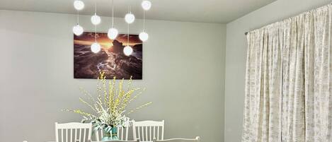 A dining area with a table set for four, a hanging light fixture, and a window with curtains.