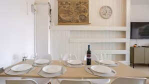 Uma sala de jantar com uma mesa posta para quatro pessoas, uma garrafa de vinho e um relógio na parede.