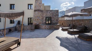 A rooftop patio with stone walls, lounge chairs, and umbrellas. - Pithos apartments is a complex of 5 full equipped apartments (Thira - Santorini)