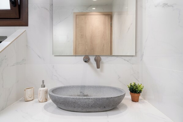 A bathroom with a large, round, gray stone sink, a wooden door, and a small potted plant.