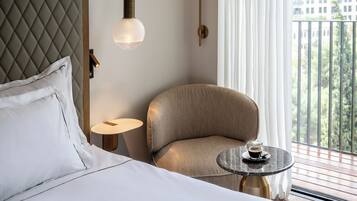 Een hotelkamer met een bed, een stoel, een klein rond tafeltje met een kopje en uitzicht op een balkon met begroeiing.